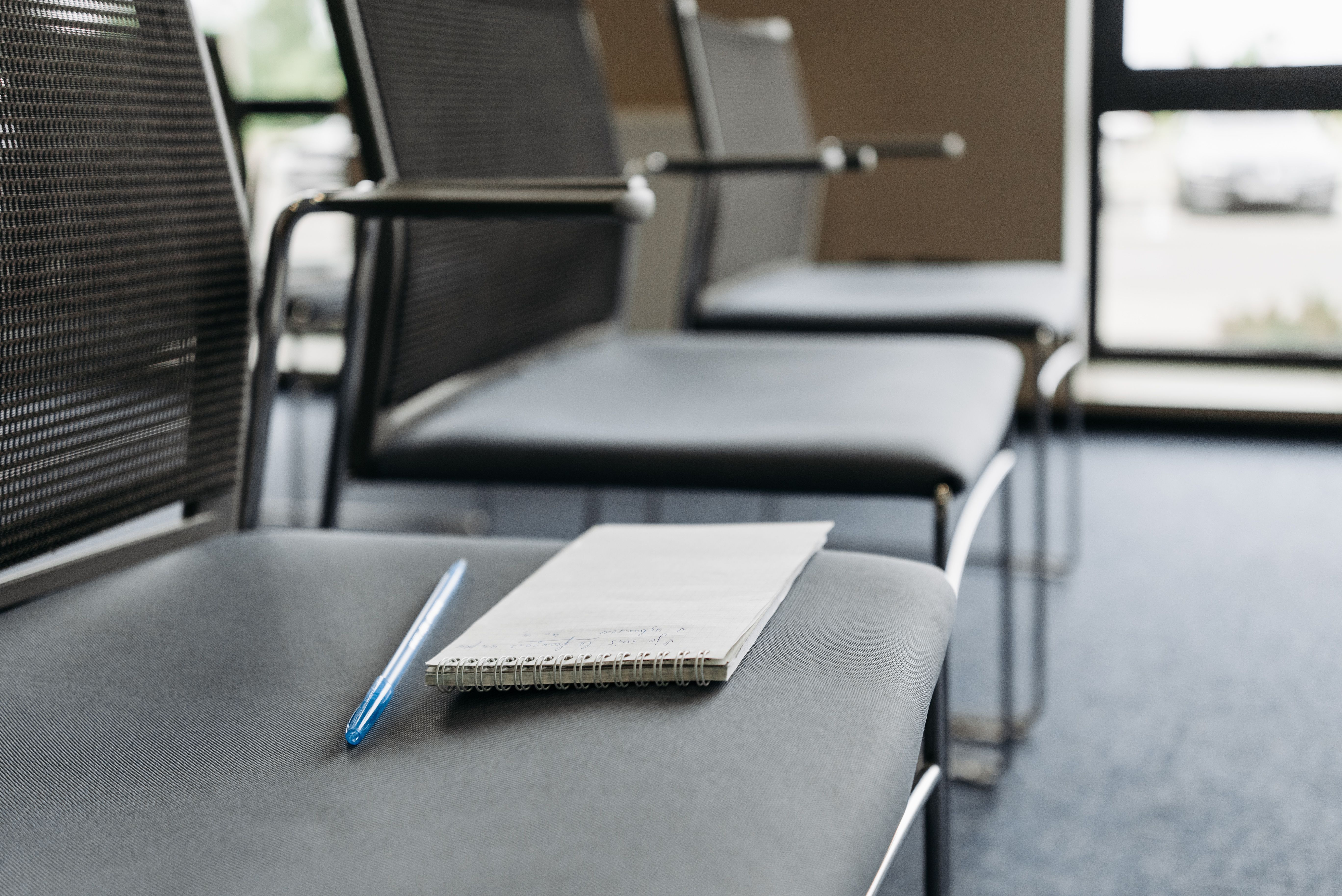 Close-up of chairs with a notebook and pen in a well-lit meeting room.