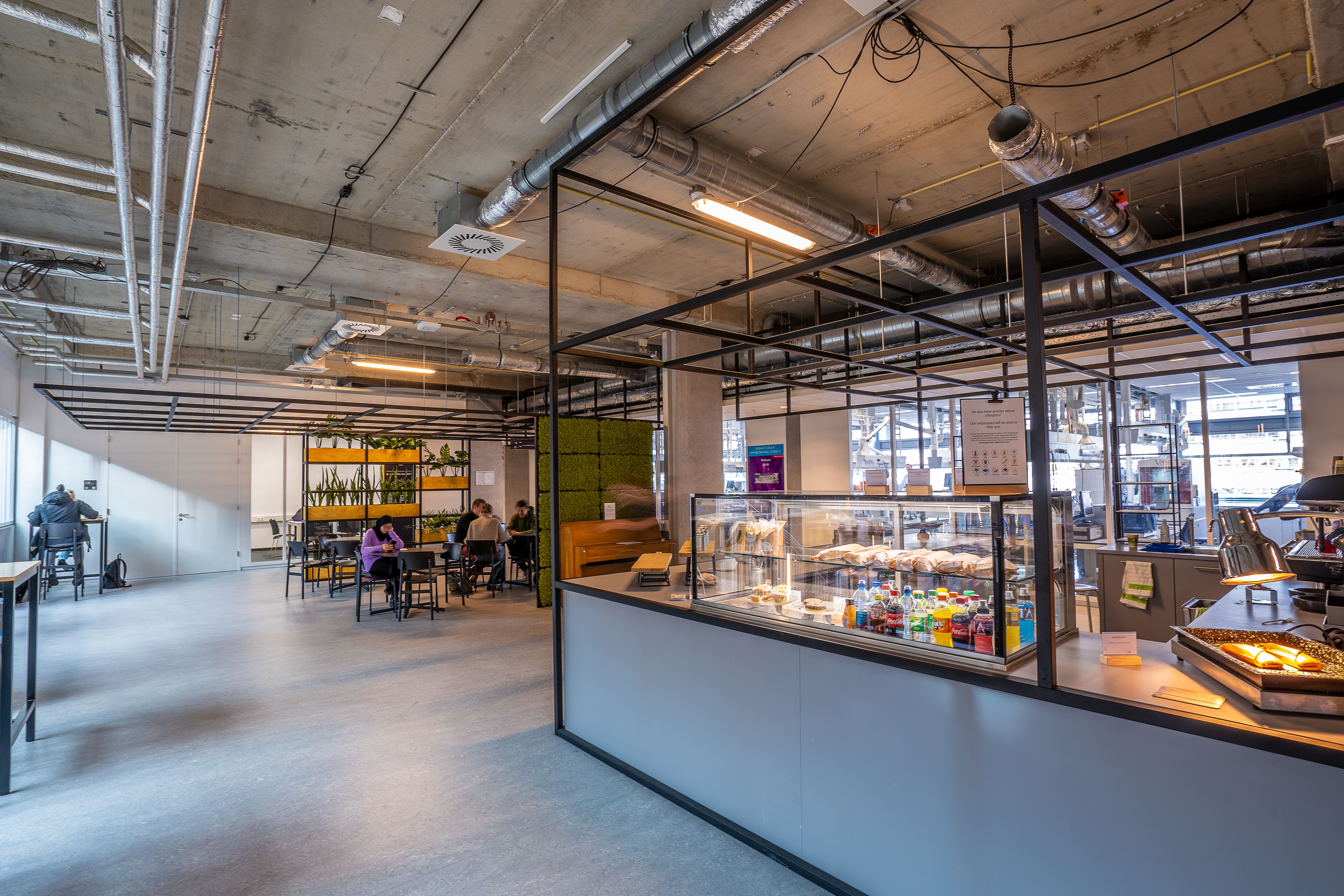 A spacious modern cafeteria with industrial design, showcasing people dining and working in a relaxed atmosphere.