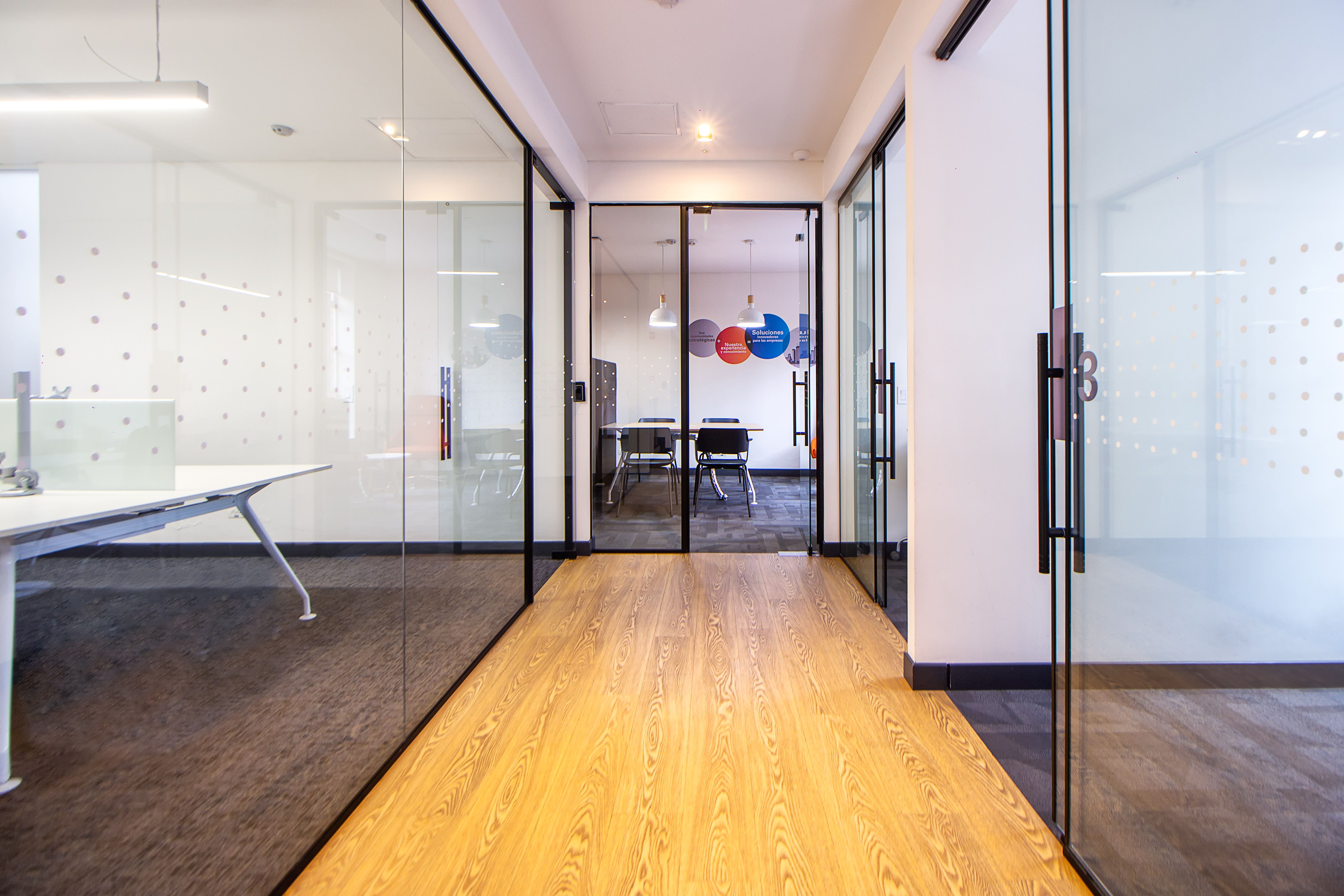 Bright modern office hallway with glass walls leading to a conference room.