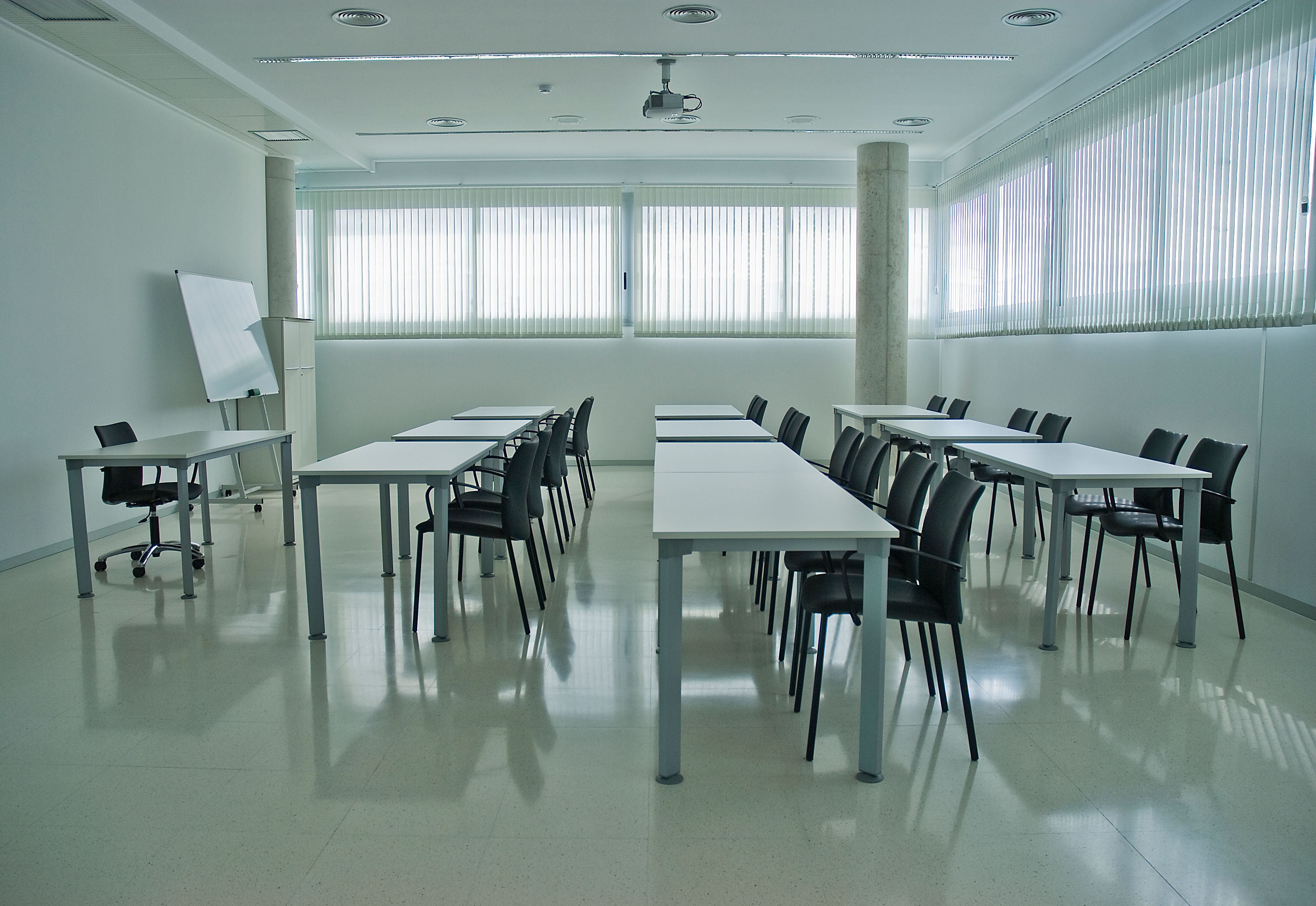 A clean, modern conference room with arranged desks, chairs, and a whiteboard.