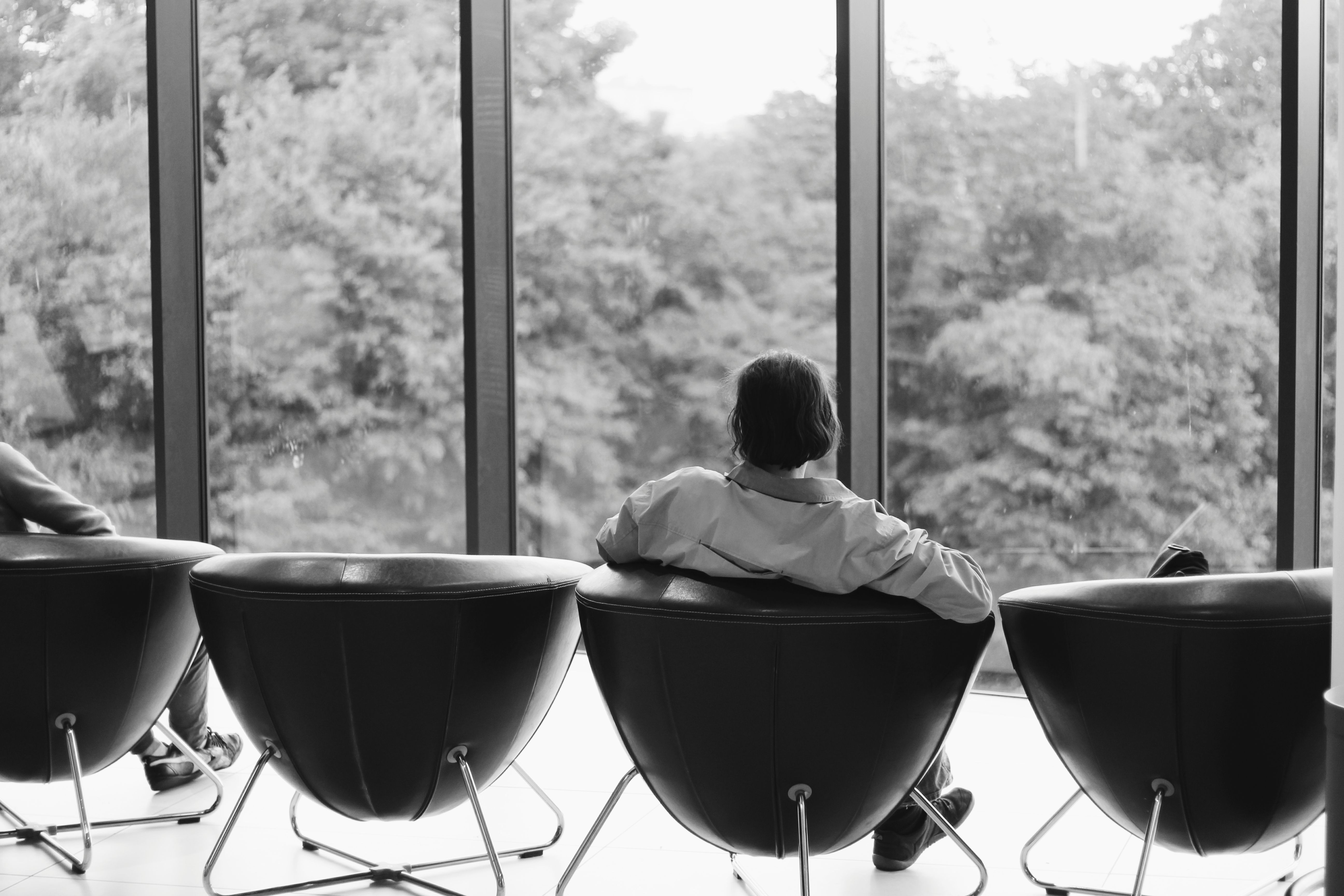 Person relaxing on modern chairs overlooking the outdoors in a minimalist room.